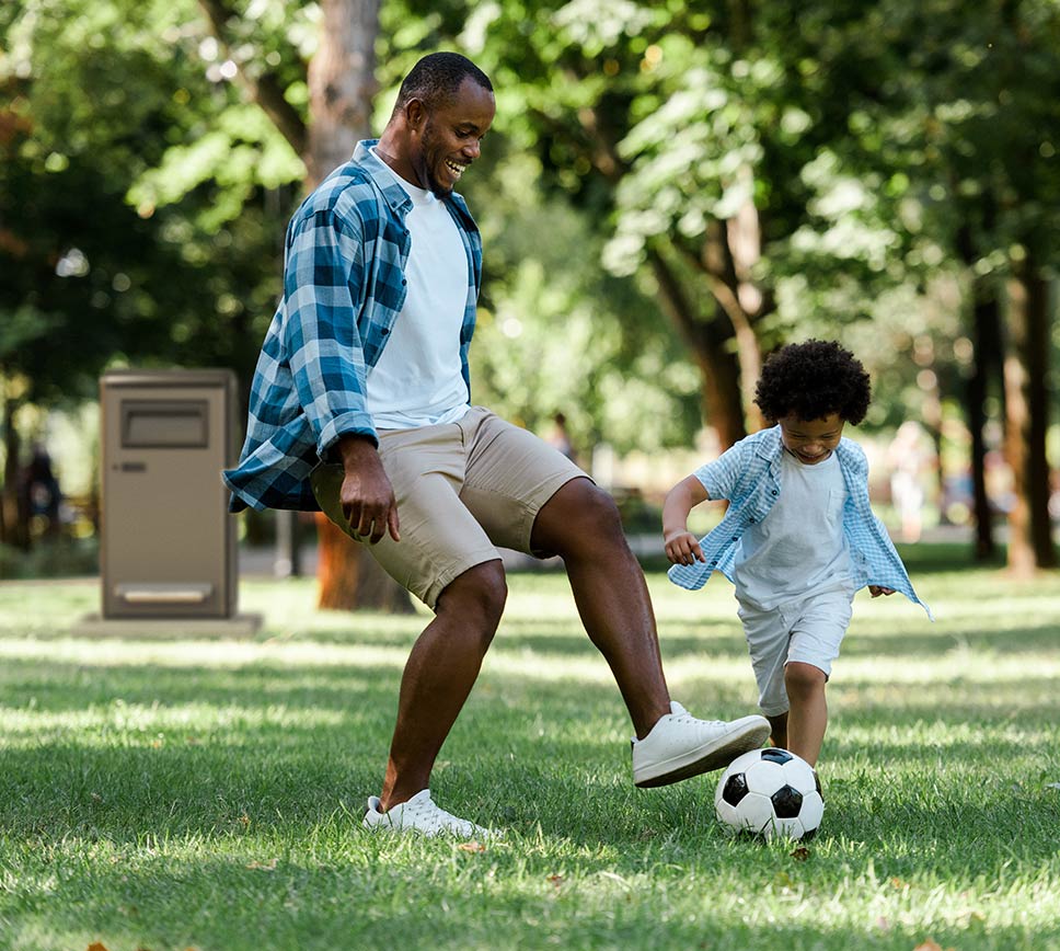 big belly trash compactor in park with family playing soccer
